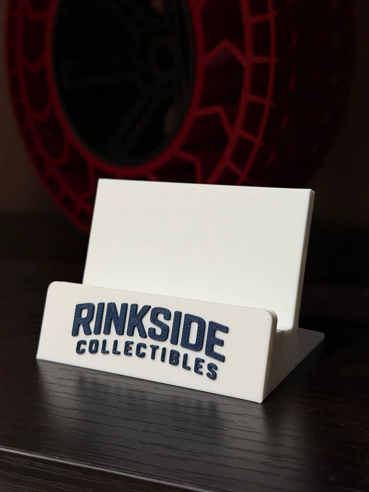 White card stand with a card shop name in raised navy lettering on the front ledge